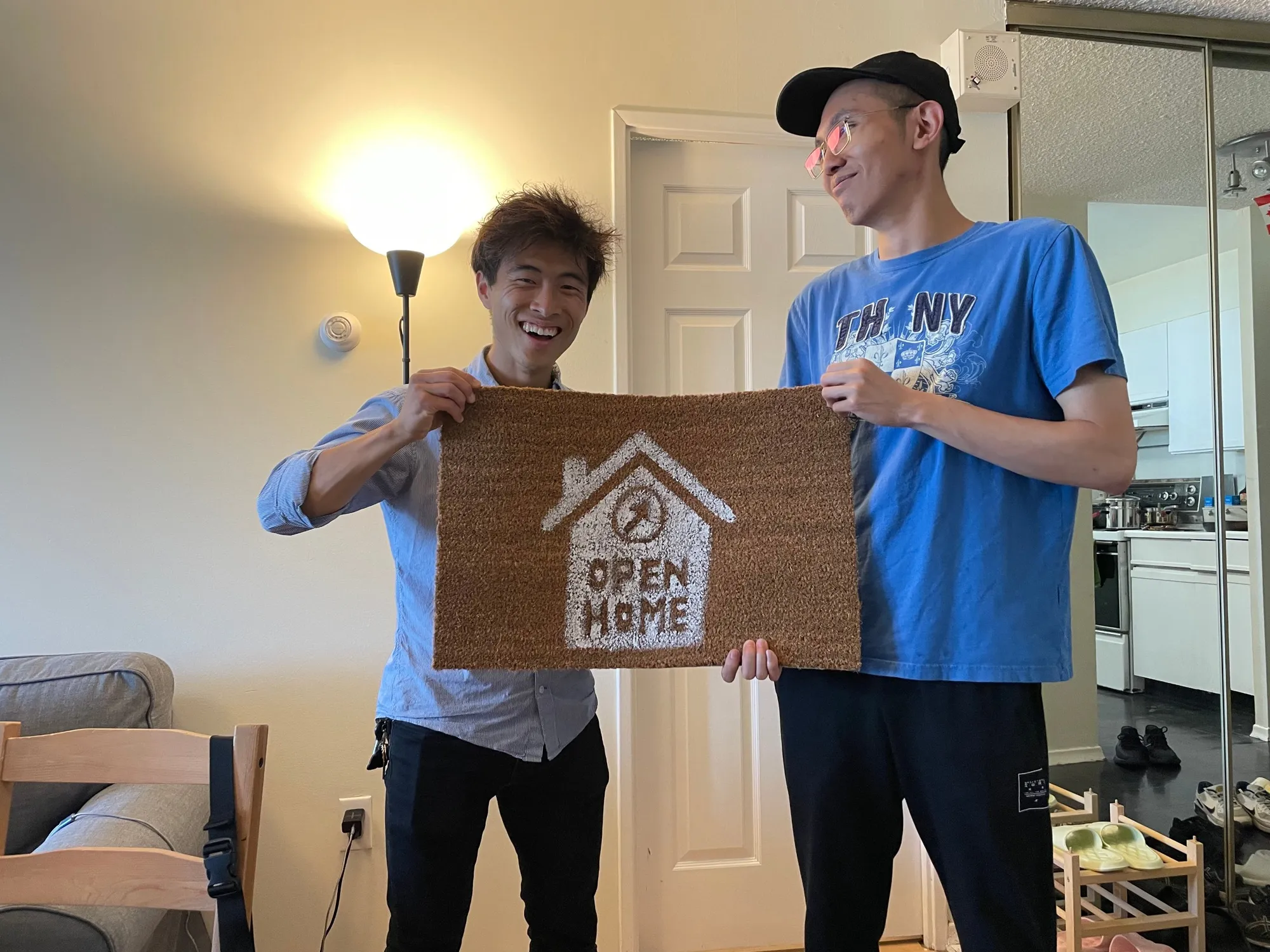 Two missionaries holding an Open Home doormat